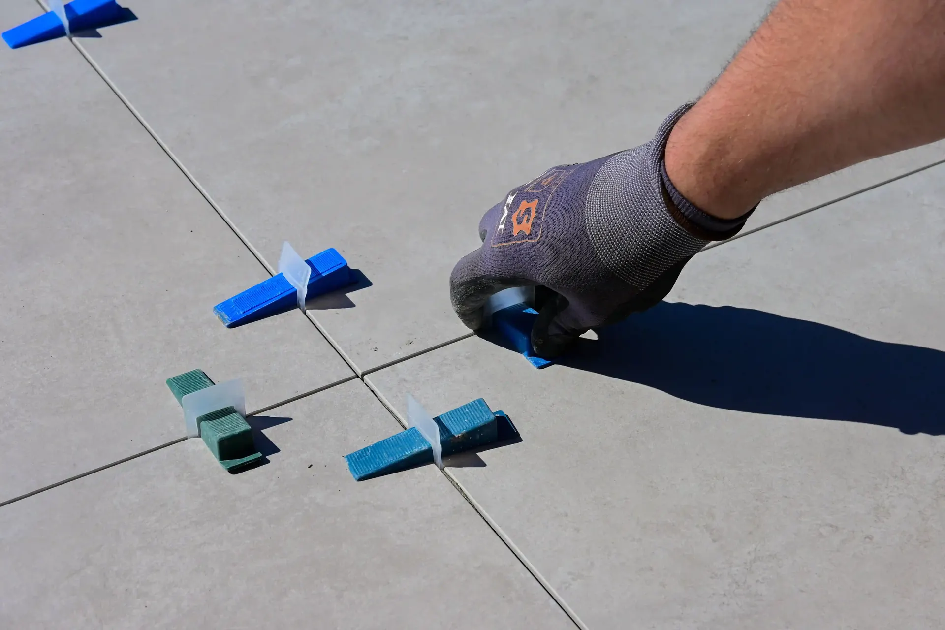 Installer placing leveling clips between large gray floor tiles