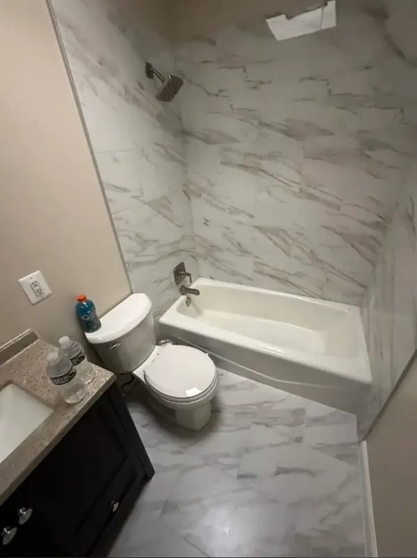 Finished: white-and-gray veined porcelain tub surround, matching floor tile and a dark vanity.