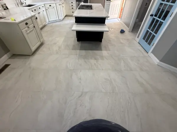 Kitchen with white cabinets and a black island on a large light-gray stone-look porcelain floor.