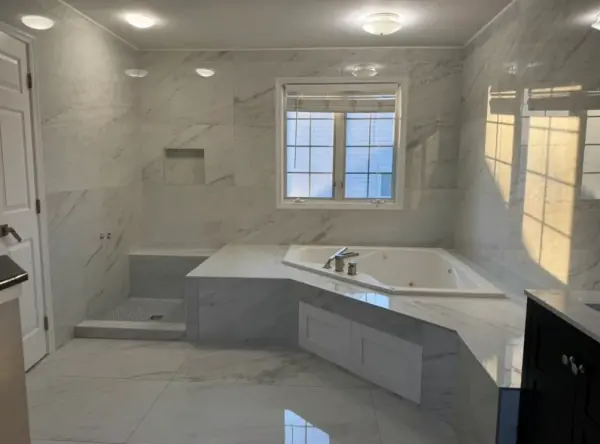 Primary bath with a tiled corner tub deck and step, veined wall tile, a recessed niche and a window above the tub.