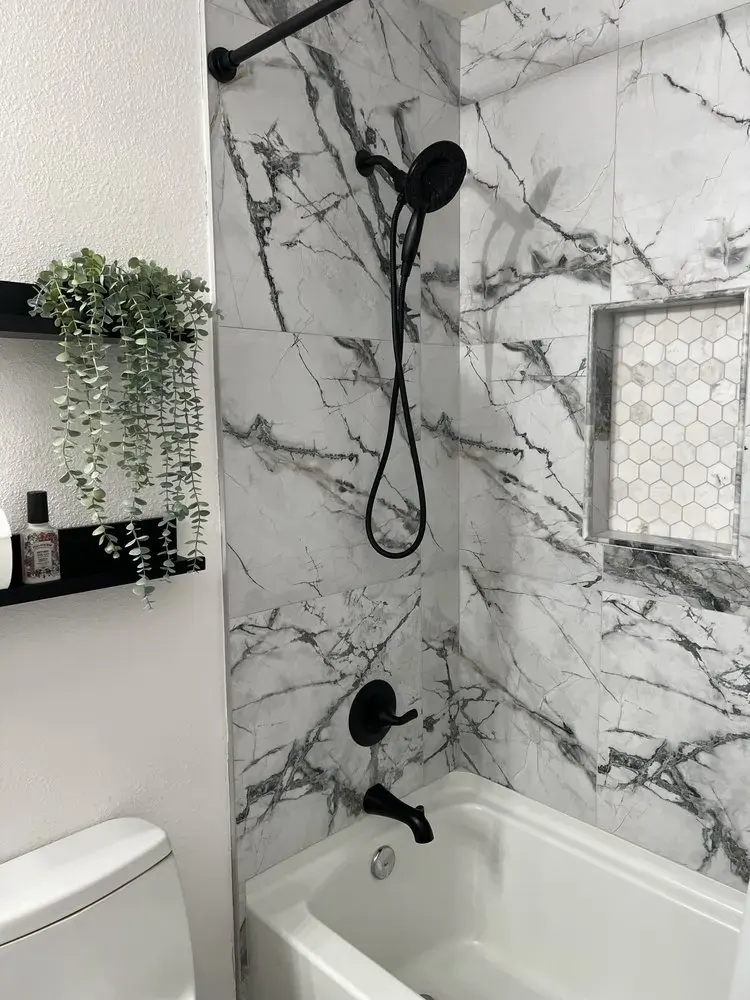 Marble-look shower wall with black fixtures and mosaic floor